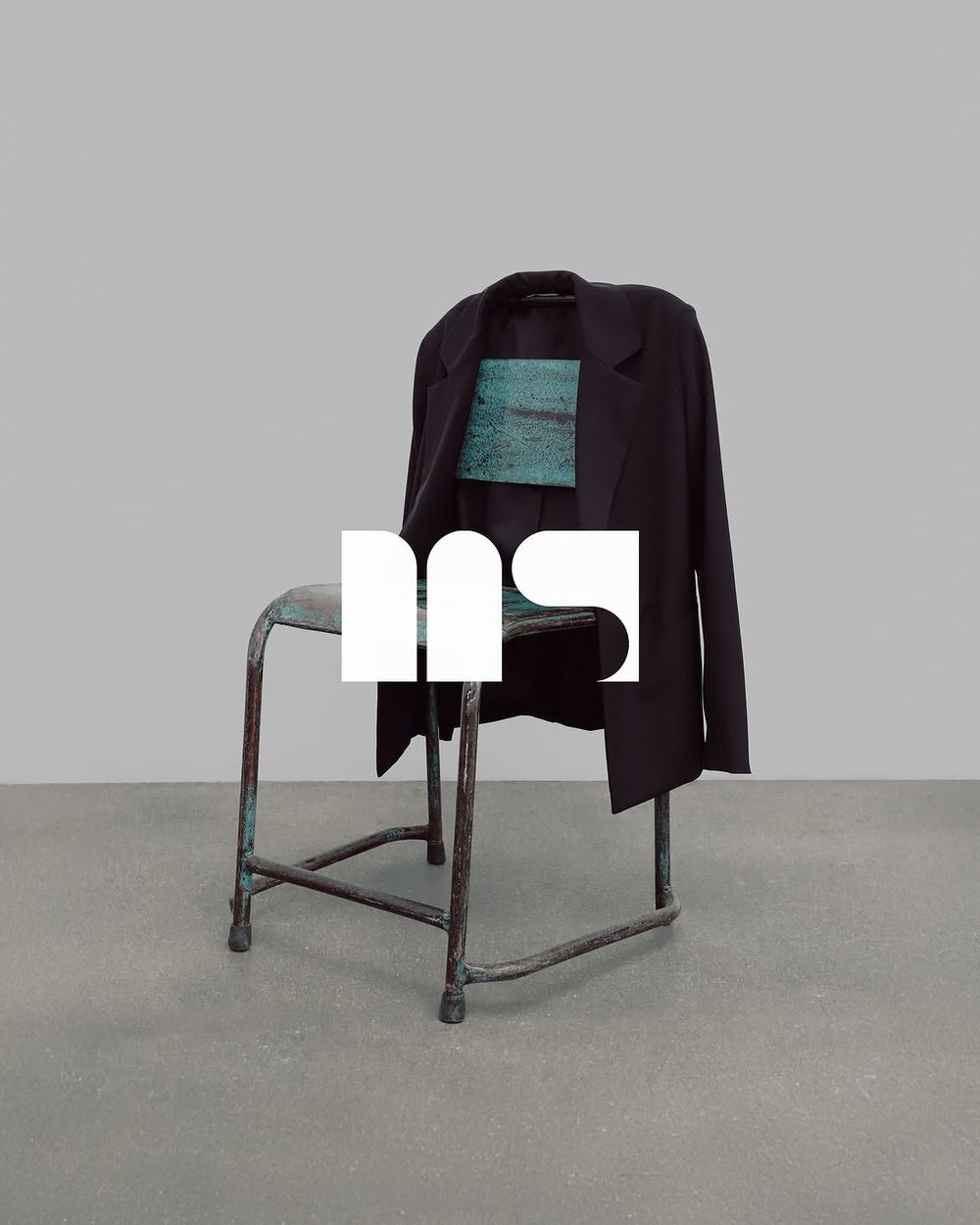 Veste noire posée sur une chaise patinée, logo MS en surimpression